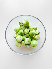 Bowl of raw Brussels sprouts on white surface. Fresh green vegetables, healthy eating, vegetarian food concept with copy space.