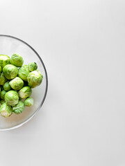 Fresh Brussels sprouts in a glass bowl on a white surface with copy space, healthy eating concept.