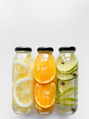 Lemon, orange, and lime detox drinks in glass bottles on white background with copy space. Concept for design and print.