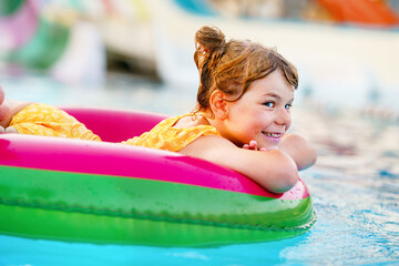 Happy little girl with inflatable toy ring float in swimming pool. Little preschool child learning...