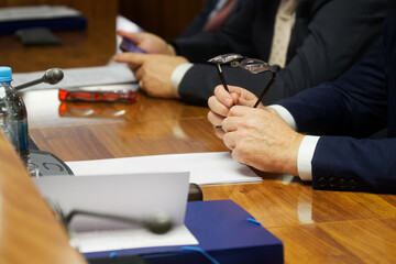 Man in a business suit holds glasses in his hands next to a document while sitting at a table with...