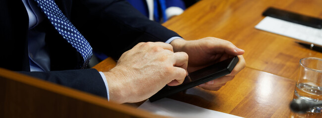 An adult male businessman in a business suit uses a mobile phone - a smartphone, sitting at a table...