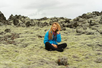 Woman traveler sits on moss in Iceland and calls on the phone.