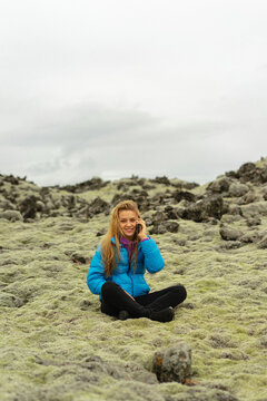 Woman traveler sits on moss in Iceland and calls on the phone.