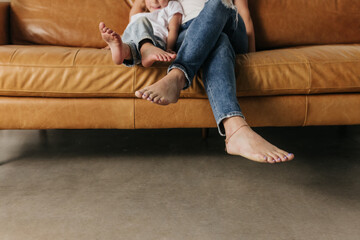 Faceless photo focus on feet of mother and daughter snuggled on couch