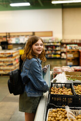 Teenage girl in a denim jacket smiling while shopping for lychee fruit