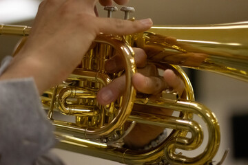 Close-up of hands playing a shiny brass mellophone.