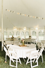 White tables and chairs in tent with bunting hanging above