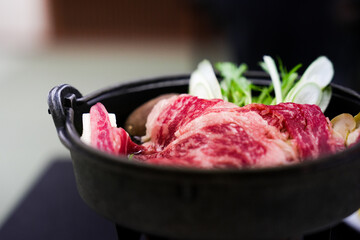 Traditional Japanese hot pot with tender premium Wagyu beef slices and fresh vegetables in a rustic cast iron pot closeup
