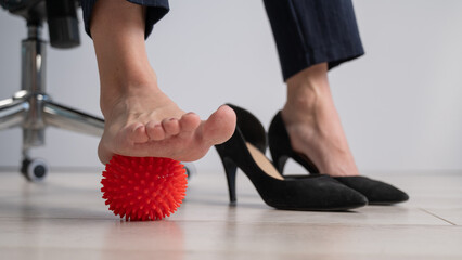Business woman massages her feet on a massage ball with spikes.