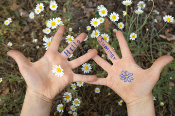 children's hands with the inscription Hello Summer written on fingers against backdrop of chamomile meadow. joy, hello holidays, relaxation, pampering, positive, cheerful childhood. energy of nature