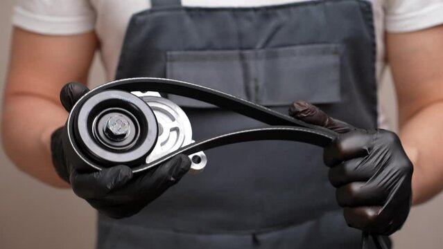 Tensioner roller and poly V-belt in hands of car mechanic. Concept of auto parts replacement, car maintenance. Sale of auto products, provision of car repair services.