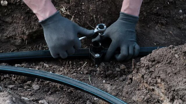 plumber installs a saddle fitting for connecting a sprinkler, automatic watering of the lawn close-up, installation of a water supply system from HDPE pipes