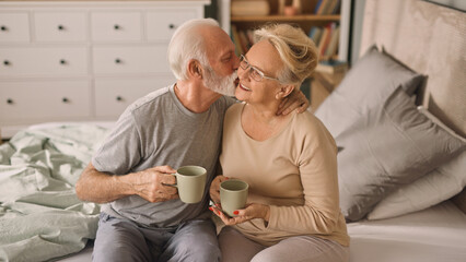 Happy elderly couple enjoying coffee or tea in bed 