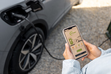 Woman using smartphone with launched application for car charging, controlling the charging process...