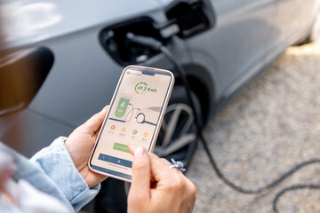 Woman using smartphone with launched application for car charging, controlling the charging process...