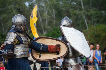 Battle of warriors tournament. Armed members of history club in knight armor demonstrating fighting...