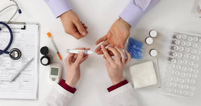 Doctor pierces patient finger with lancet top view