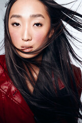 Stylish Asian woman in a vibrant red leather jacket with flowing hair against a windy backdrop