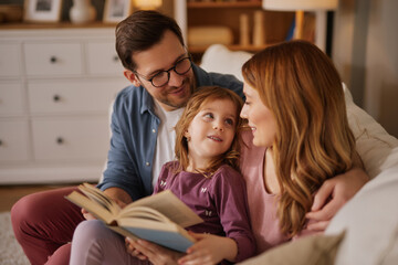 Family with little daughter reading book on sofa in living room