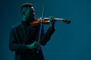 Talented young African American man playing violin with passion and skill against a dark blue...