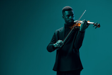 Elegant man in black suit playing the violin against vibrant blue background in stock photo