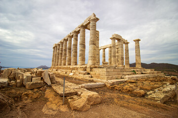 Fototapeta premium Majestic Ruins of the Ancient Temple of Poseidon at Cape Sounion Under Cloudy Skies Overlooking the Aegean Sea