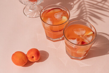Healthy summer iced fruit drinks, apricots and peaches, iced fruit peach cocktails on pastel pink background with bright sunlight and floral shadows