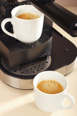 Two cups of espresso under the coffee maker on kitchen table.