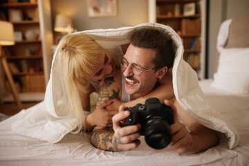 Woman photographing her tattooed husband with a camera in bed