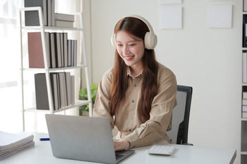 Young woman working indoor and using laptop, headset with happy and smile face.