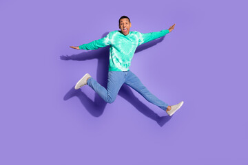 Fototapeta premium Full length photo of funky cool guy dressed turquoise sweatshirt jumping high emtpy space isolated violet color background