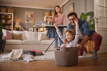 Little girl and dad laughing while playing with the laundry basket in living room