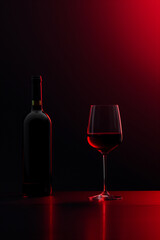 Glass with red wine and bottle on a black-red background