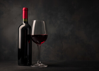 Glass with red wine and bottle next to it on a black background
