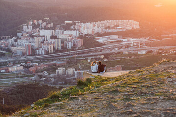 Happy young couple watching the sun set over the bay behind the city, wearing casual clothing