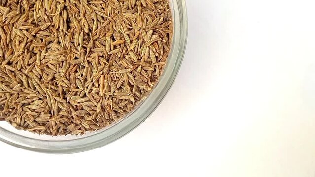 Cumin seeds in a glass bowl isolated rotating top left corner, a glass bowl full of Cumin seeds on white background, close up, herbs and spices