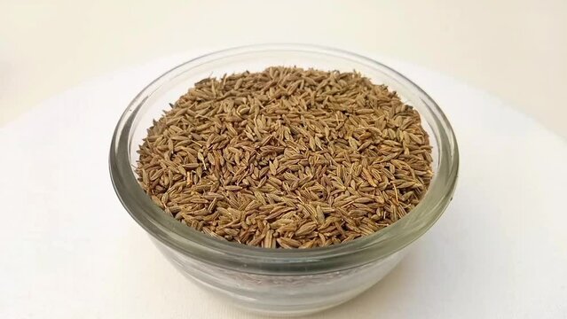 Cumin seeds in a glass bowl isolated rotating on white background, a glass bowl full of Cumin seeds in the center frame, zooming in, close up, herbs and spices