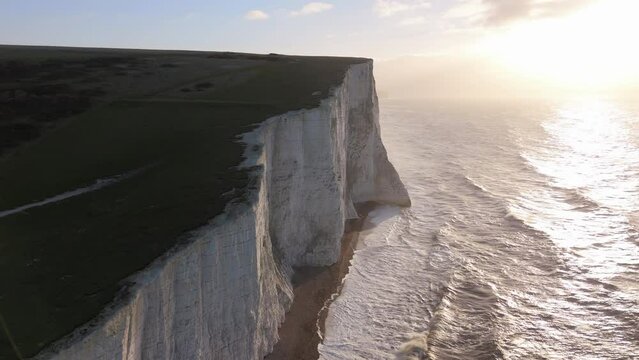 Majestic white cliffs overlook the ocean, with golden light of sunset. Waves crash dramatically below, creating a serene and picturesque landscape that captivates nature enthusiasts. Seven Sisters 