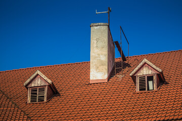 The roof of a house has a chimney and two windows with shutters