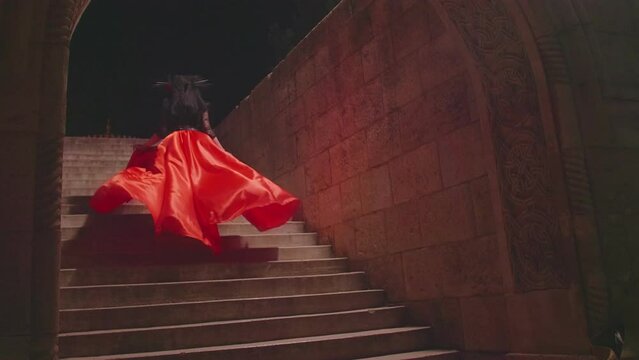 Slow motion of Women in the guise of Holy Death in a magnificent red dress ascends the stone steps against the backdrop of a stone wall. Traditional Dia de Los Muertos Festival in Mexico