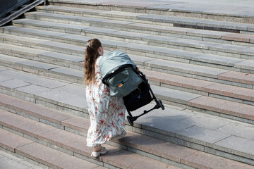Woman carries a stroller up the stairs, mother with baby pram on city street