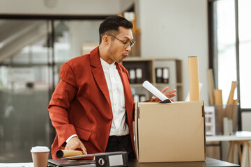 A middle-aged Asian businessman in a formal suit is working at his desk, preparing to resign after...
