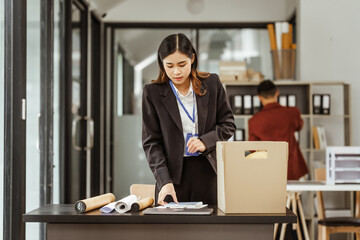A young Asian businesswoman in a formal suit is working at her desk, preparing to resign after...
