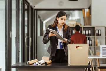 A young Asian businesswoman in a formal suit is working at her desk, preparing to resign after...