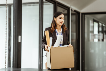 A young Asian businesswoman in a formal suit is working at her desk, preparing to resign after...