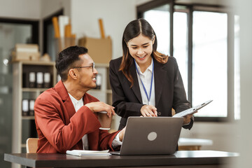 Middle-aged businessman and young Asian businesswoman work together at their desks, cooperation, collaboration, communication. teamwork, partnership, coordination to achieve mutual success.