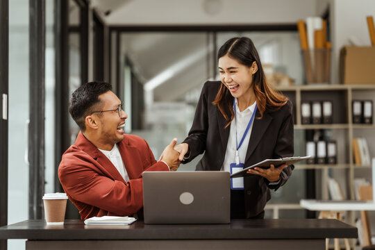 Middle-aged businessman and young Asian businesswoman work together at their desks, cooperation, collaboration, communication. teamwork, partnership, coordination to achieve mutual success.