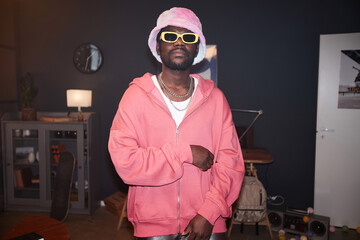 Waist up portrait of Black young man wearing pink outfit hip-hop style and looking at camera with...
