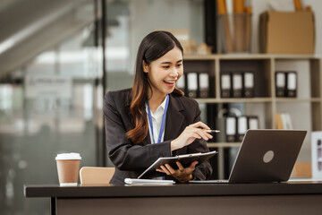 A young Asian businesswoman is seen diligently working at her desk. She's immersed in tasks ranging...